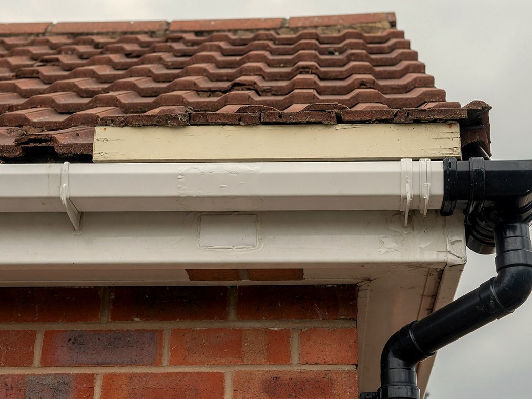 White gutter and black downpipe at the eaves of a brick house with a tiled roof
